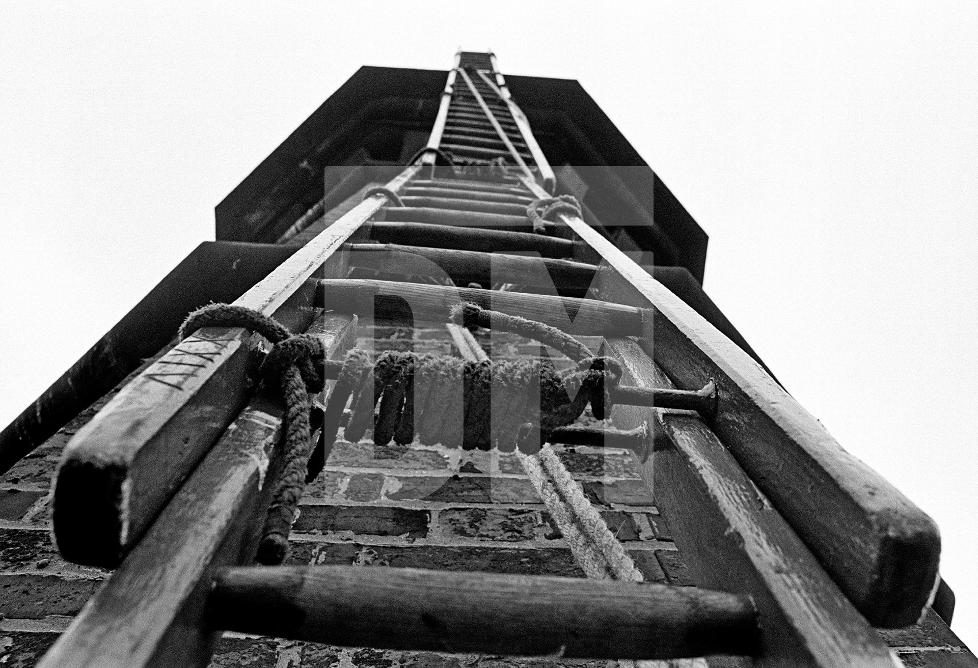 Looking up at the oversailer from just beneath the lower string course. Ladders are all in place with lashings clearly visible. September 1976 by Daniel Meadows