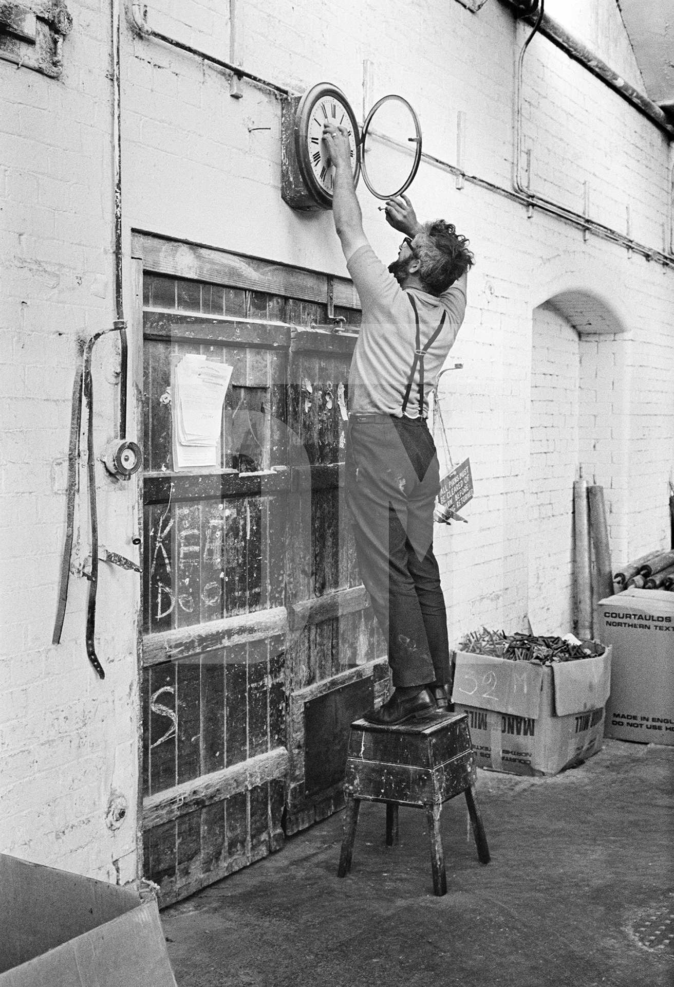 In the weaving shed. Stanley Graham, mill engineer, winding clock. August 1976 by Daniel Meadows