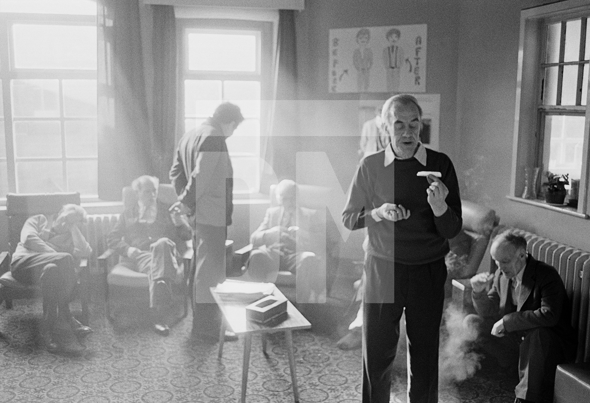 In the day-room, Stanley Massey aged 57 (foreground) rolls a cigarette, Clayton Ward, Prestwich Psychiatric Hospital, Manchester. February 1978 by Daniel Meadows