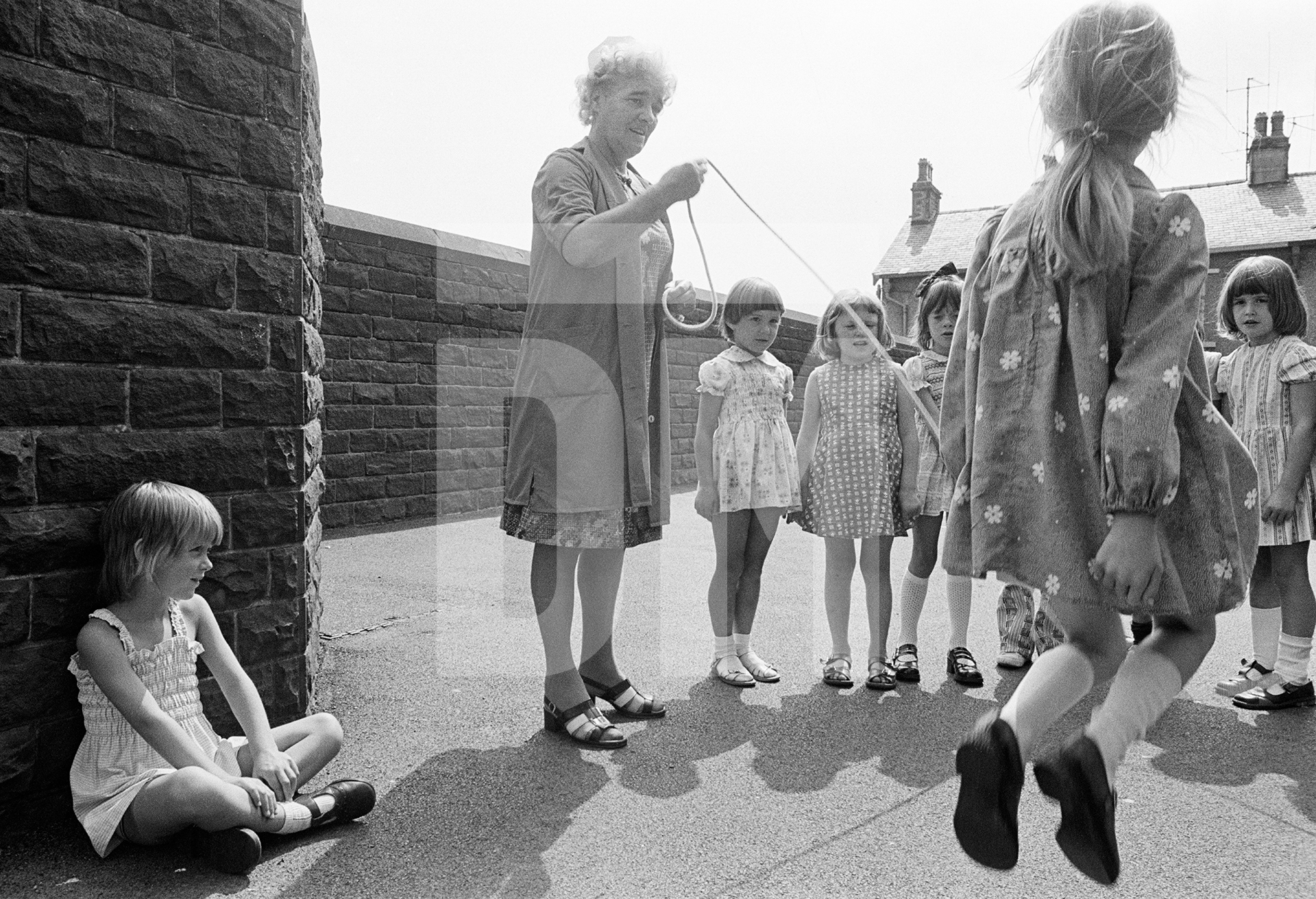 Dinner lady, with children skipping, Church of England County Primary School, Barrowford, Lancashire. August 1976 by Daniel Meadows