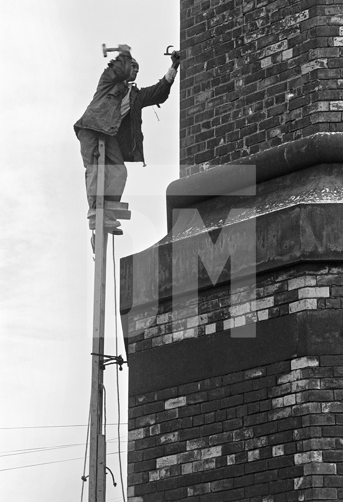 With the first ladder in place, Peter hammers in a ‘dog’ to begin fixing the second ladder. September 1976 by Daniel Meadows