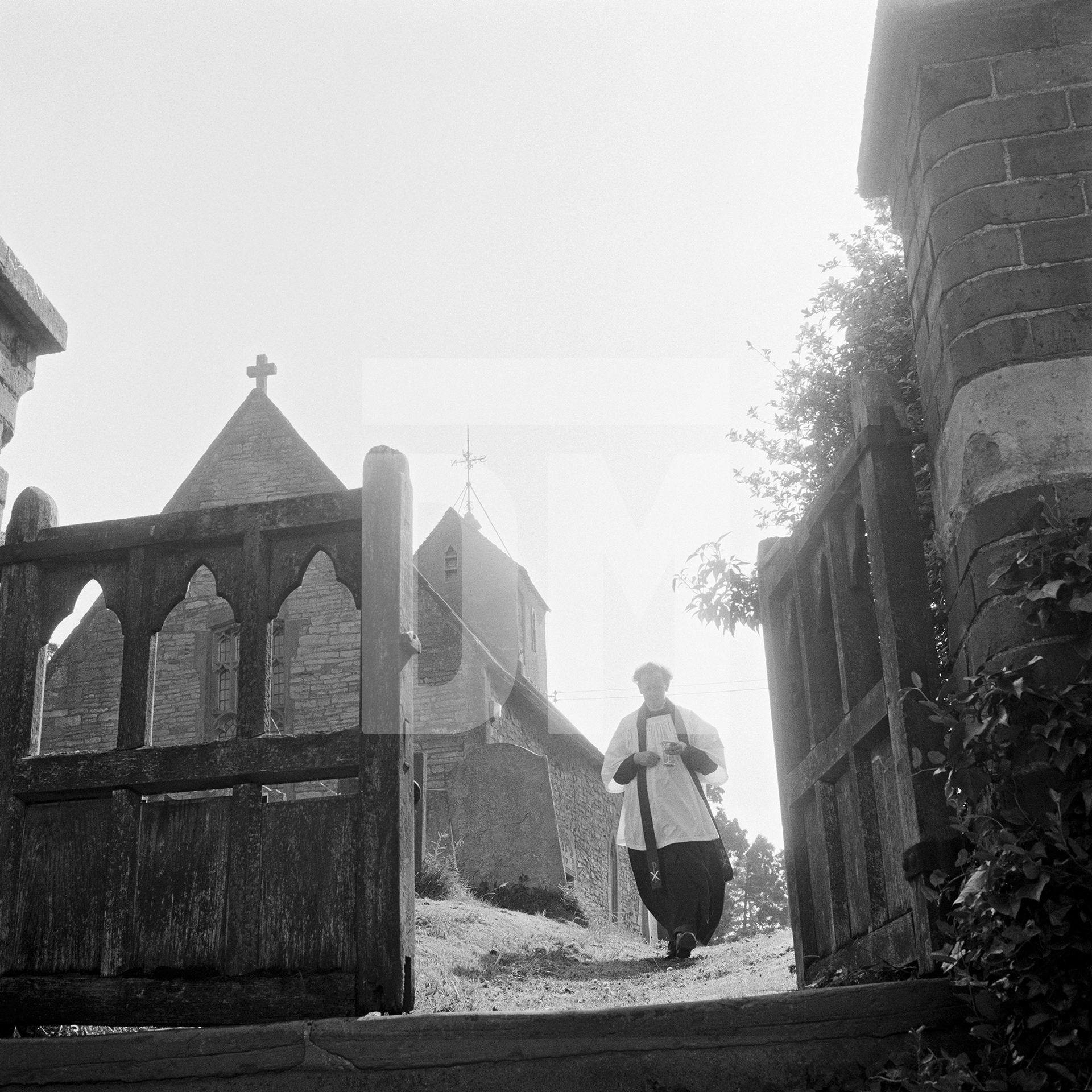 Vicar taking communion to parishoner out in the village during Sunday church service. Great Washbourne, Gloucestershire. July 1974 by Daniel Meadows