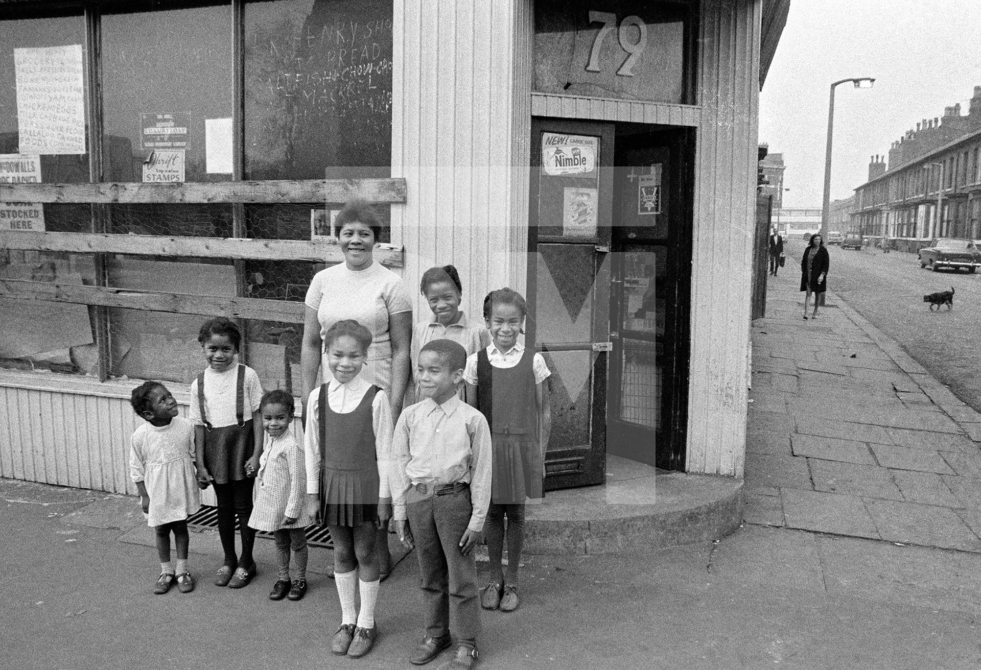 Caribbean food store, 79 Greame Street. The sign in the window reads ‘Henry Shop, Bread, Fish, Chow-Chow, Mackrel...’ Left-to-right: Sharon Henry, Michelle Henry, Pauline Crooks, Monica Crooks, Mrs Violet Henry, Freddy Crooks, Janet Henry, Sandra Crooks. Moss Side, Manchester. 1972 by Daniel Meadows