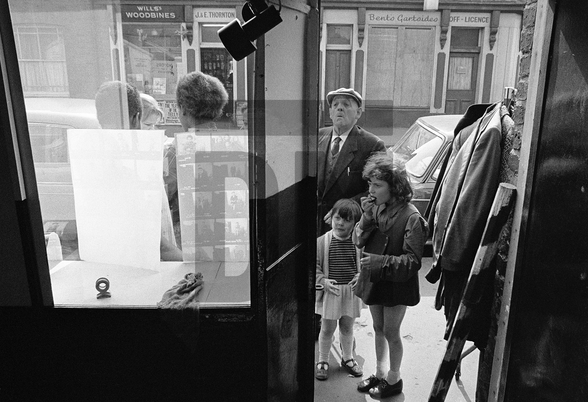 Watching as new pictures are posted in the window of The Shop on Greame Street, Moss Side, Manchester. February-April 1972 by Daniel Meadows