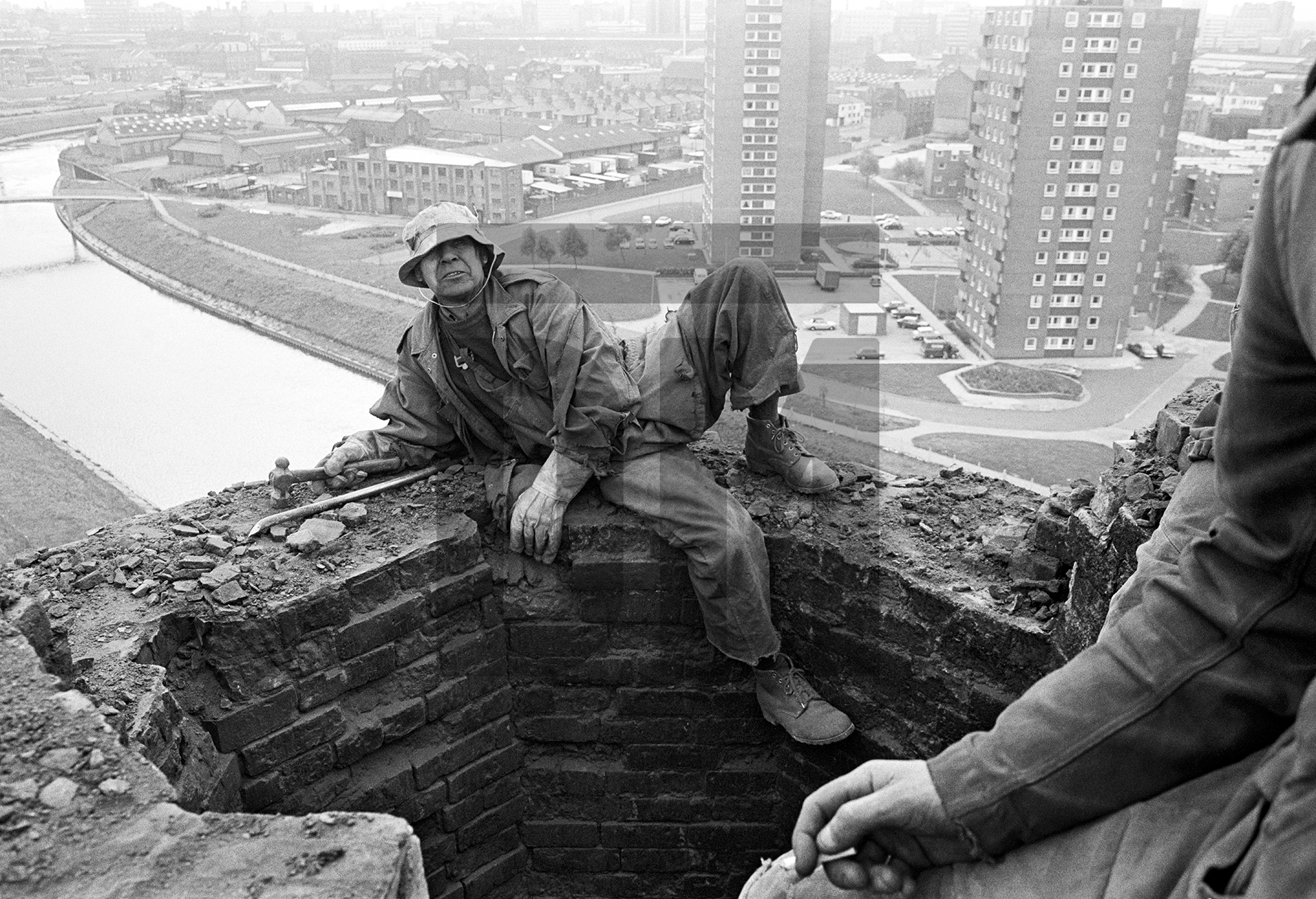 150 feet up, atop of the stack and shortly after starting the demolition process, Peter Tatham steeplejack poses for his portrait. September 1976 by Daniel Meadows