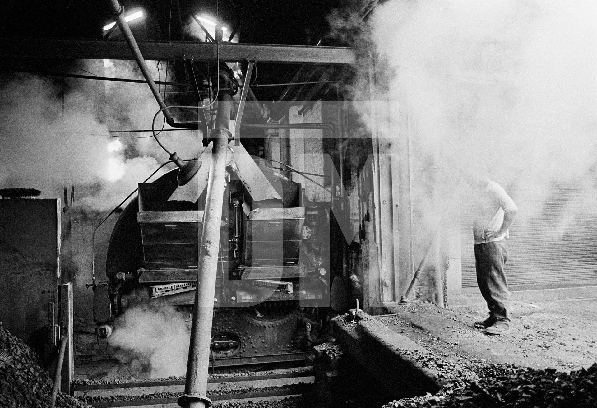 Stanley Graham, engineer, ‘blowing off’ and ‘blowing down’ the Lancashire boiler (emptying it) ready for fluing. Wakes holiday, July 1976 by Daniel Meadows