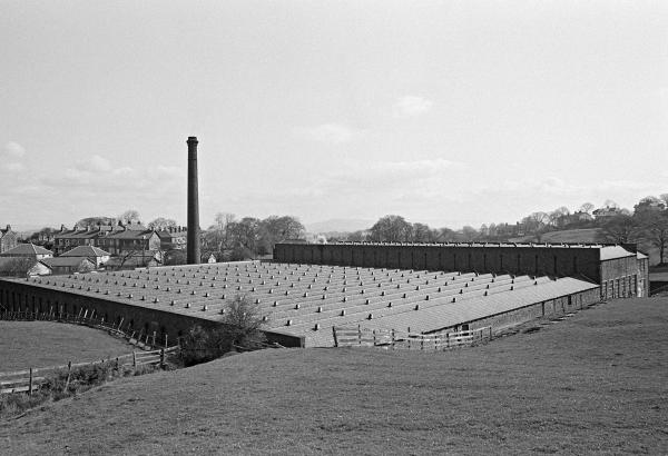View from the southwest. The slate roof of the weaving shed with the warehouse beyond. The chimney is positioned midway along the northern side. April 1976