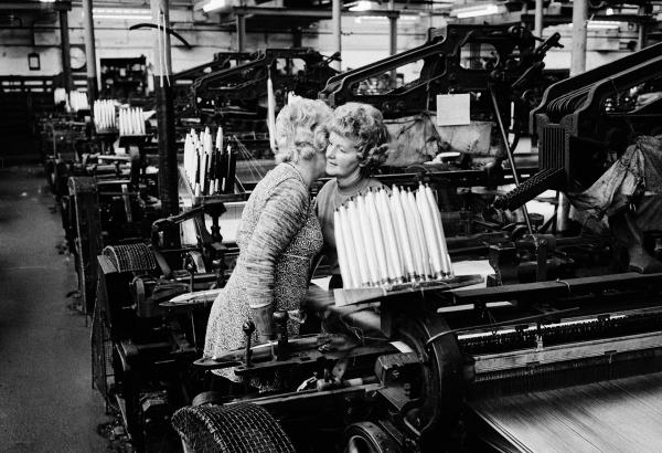 Two weavers in conversation, their faces close together so they can chat privately above the 'clatter' (deafening noise) of the looms without others nearby, skilled lip-readers all, being able to follow their conversation, Spring Bank Mill, Fence. Autumn 1975