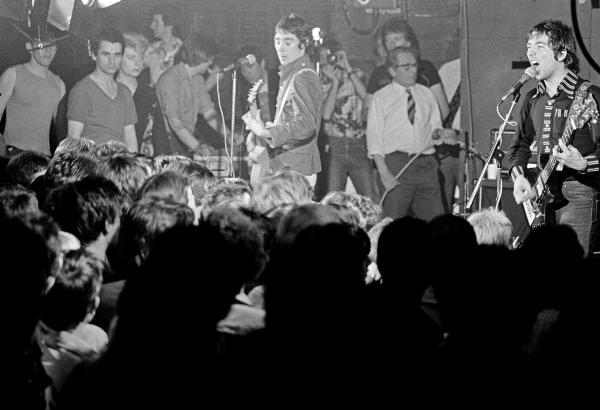 Buzzcocks (with photographer Kevin Cummins immediately behind singer/guitarist Pete Shelley, centre) at the Russell Club, Hulme, for a 'Factory' night. 'What's On' programme from Granada TV on location. April 1979