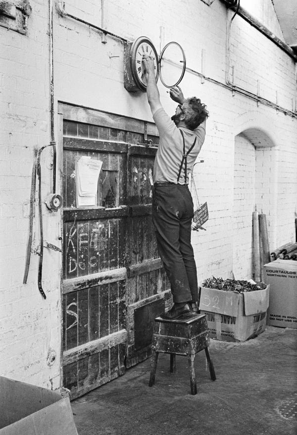 In the weaving shed. Stanley Graham, mill engineer, winding clock. August 1976