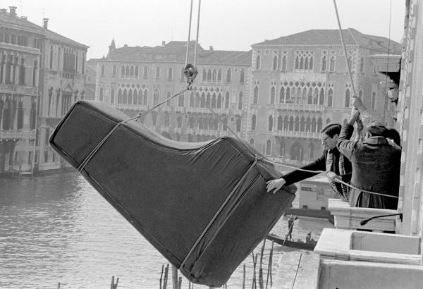 Tony Palmer [director] steadies a piano above the Grand Canal during filming of 'Wagner'. Venice 1982