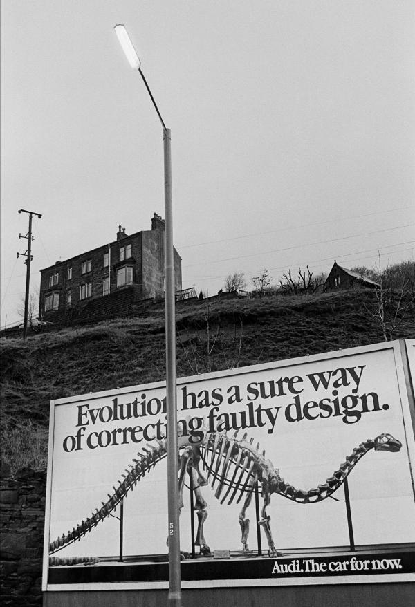 Dinosaur, billboard, street lamp, row of terraces, West Yorkshire. December 1979