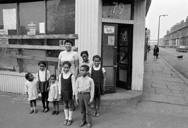 Caribbean food store, 79 Greame Street. The sign in the window reads ‘Henry Shop, Bread, Fish, Chow-Chow, Mackrel...’ Left-to-right: Sharon Henry, Michelle Henry, Pauline Crooks, Monica Crooks, Mrs Violet Henry, Freddy Crooks, Janet Henry, Sandra Crooks. Moss Side, Manchester. 1972
