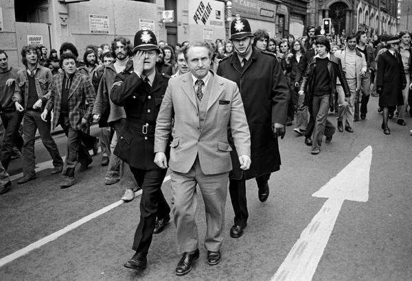 Anti Nazi League (ANL) demonstration against a National Front (NF) meeting. George Wright, NF Parliamentary candidate for Rotherham in the 1976 by-election (1,696 votes), is escorted by police through demonstrators, policeman wiping spittle from his face, Leeds. April 1978
