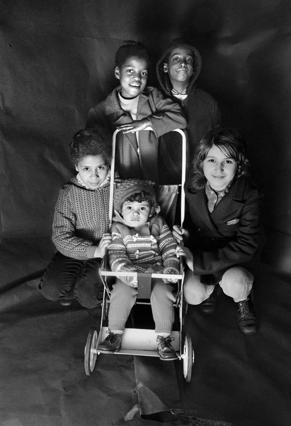 Antoinette Robotham (later Anjee McPherson) and Neville Robotham (later Neville Davis), standing. Debra Caines, crouching left, her sister Tricia in pushchair, Crouching right Wanda Bendix. Group portrait from The Shop on Greame Street, Moss Side, Manchester. February-April 1972