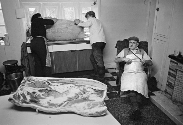 Elsie Richardson and Tony Critchley wash salt off a bacon flitch, Cyril Richardson sharpens his knife. North Yorkshire 1976